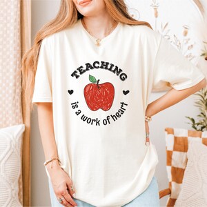 a woman wearing a teaching is a work of heart t - shirt