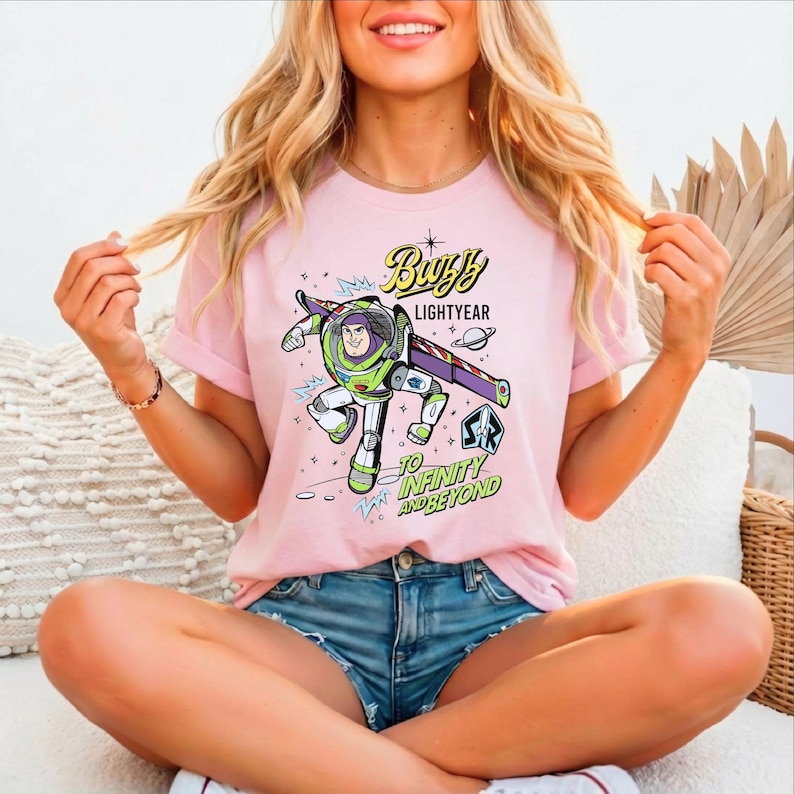 A woman wearing a pink t-shirt with a graphic of Buzz Lightyear from the Toy Story franchise, sitting cross-legged on a couch.