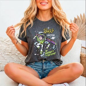A smiling woman wearing a t-shirt with a character from the Toy Story franchise, specifically Buzz Lightyear, sitting cross-legged on a couch.