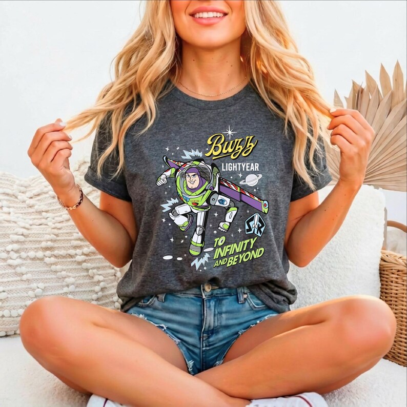 A smiling woman wearing a t-shirt with a character from the Toy Story franchise, specifically Buzz Lightyear, sitting cross-legged on a couch.