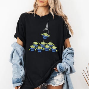 A woman wearing a black t-shirt with a graphic of a group of green alien characters.