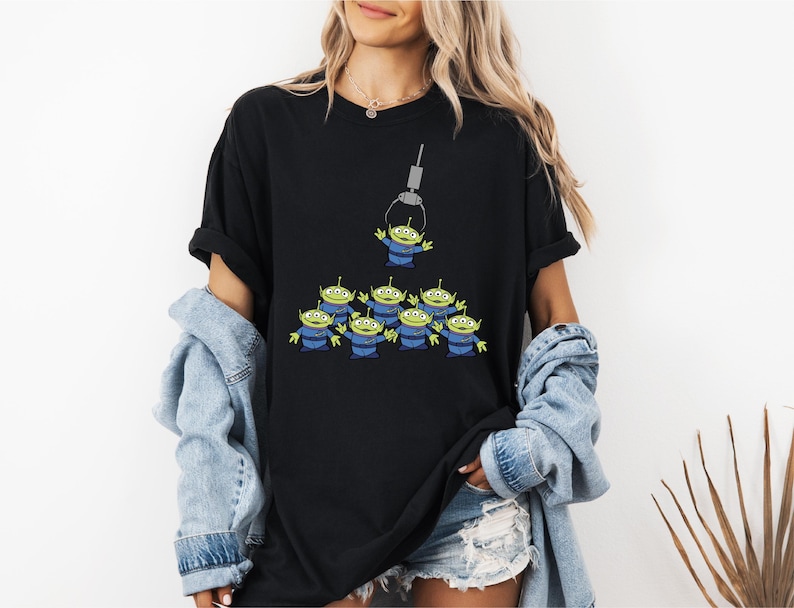 A woman wearing a black t-shirt with a graphic of a group of green alien characters.