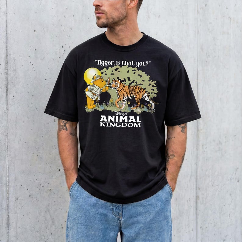 A man wearing a black t-shirt with a graphic design featuring a tiger and Winnie the Pooh characters from the Disney animated film "Animal Kingdom".