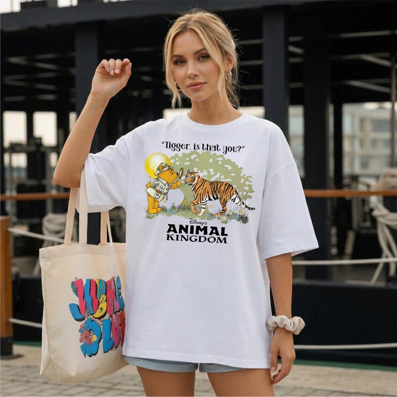 A woman wearing a white t-shirt with a cartoon tiger and text, standing in front of a building.