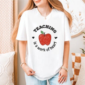 a woman wearing a teaching is a work of heart t - shirt