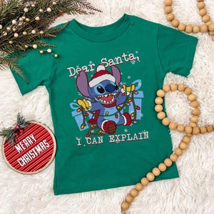 a green t-shirt with a cartoon character and text, along with Christmas decorations such as a Christmas tree, ornaments, and beads.