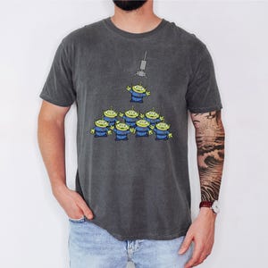 A man wearing a gray t-shirt with a graphic of a group of alien characters.