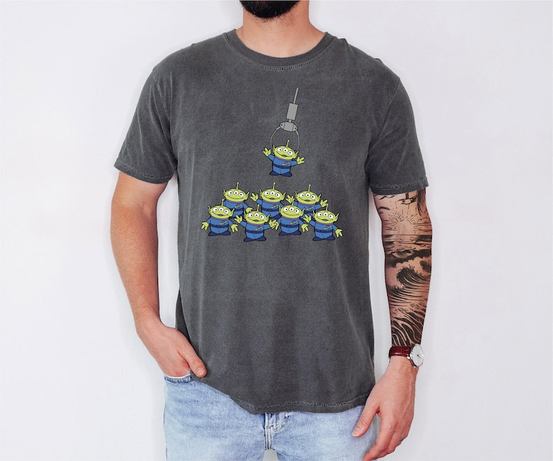 A man wearing a gray t-shirt with a graphic of a group of alien characters.