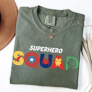 a t - shirt that says superhero squad next to a hat