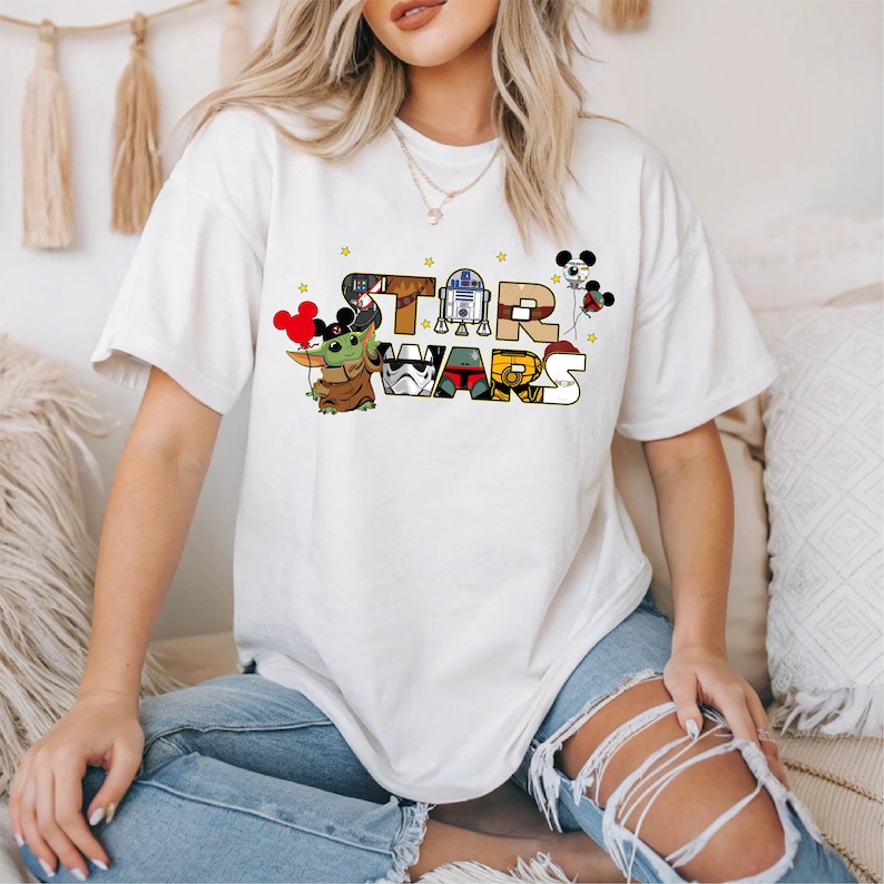 A woman wearing a white t-shirt with a Star Wars graphic design, including characters and text.