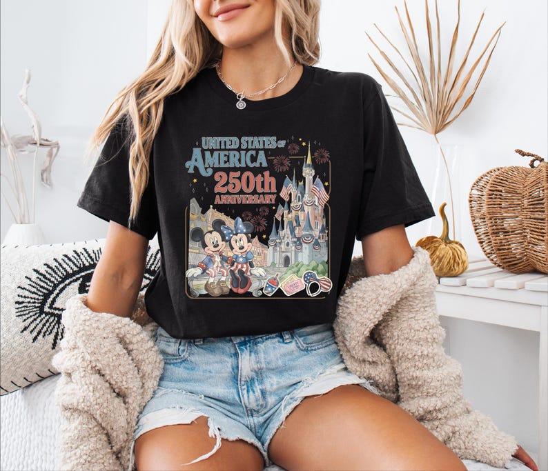 A woman wearing a black t-shirt with a graphic design celebrating the United States' 250th anniversary, featuring Mickey Mouse and other iconic Disney characters.