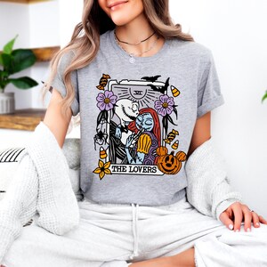 A woman wearing a grey t-shirt with a graphic design featuring characters from the movie "The Jack Skellington".