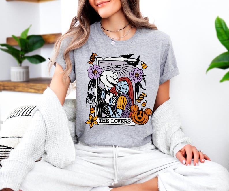 A woman wearing a grey t-shirt with a graphic design featuring characters from the movie "The Jack Skellington".
