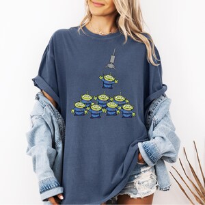 A woman wearing a blue t-shirt with a graphic of a group of alien characters and a denim jacket.