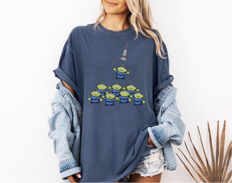 A woman wearing a blue t-shirt with a graphic of a group of alien characters and a denim jacket.