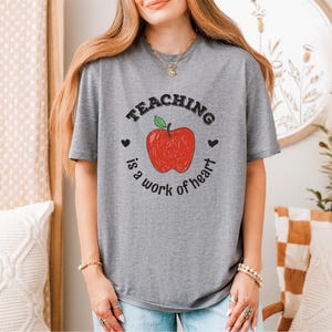 a woman wearing a teaching is a work of heart t - shirt