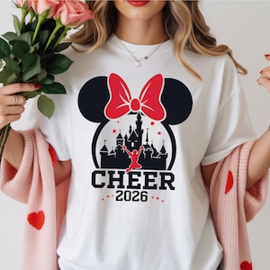 A woman wearing a white t-shirt with a graphic design of a castle and a red bow, holding a bouquet of pink roses.