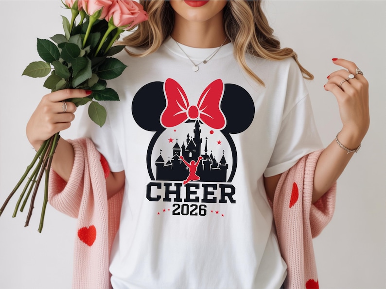 A woman wearing a white t-shirt with a graphic design of a castle and a red bow, holding a bouquet of pink roses.