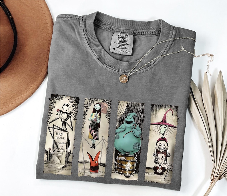 May include: Gray Comfort Colors t-shirt featuring four panels with characters from The Nightmare Before Christmas. The panels include Jack Skellington, Sally, Oogie Boogie, and the Mayor. A silver necklace with a pendant is also visible.