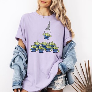 A woman wearing a purple t-shirt with a graphic of a group of alien characters being held by a claw-like device.