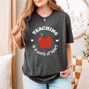 a woman wearing a teaching is a work of heart t - shirt