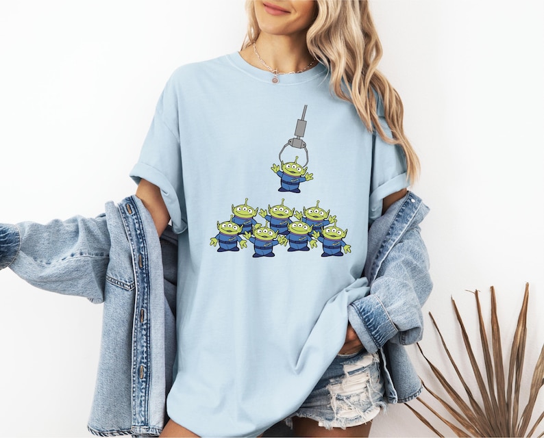 A woman wearing a light blue t-shirt with a graphic of a group of alien characters being lifted by a crane.