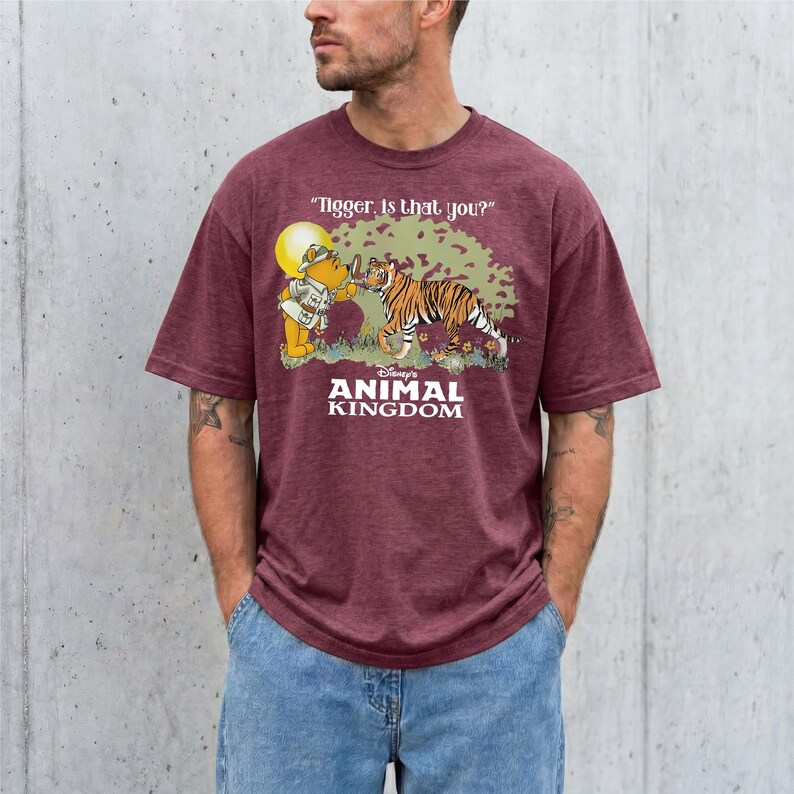 A man wearing a maroon t-shirt with a graphic design depicting a tiger and Winnie the Pooh characters from the Disney animated film "Animal Kingdom".