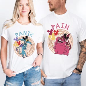 Puede incluir: Dos camisetas blancas con un gráfico de personaje de dibujos animados y texto. La camiseta de la izquierda dice "PANIC" y presenta un personaje azul con una cola de diablo y orejas de Mickey Mouse. La camiseta de la derecha dice "PAIN" y presenta un personaje rosa con una cola de diablo y orejas de Mickey Mouse.
