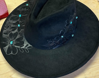 May include: A black felt fedora hat with a wide brim and a floral design. The hat is decorated with turquoise stones.
