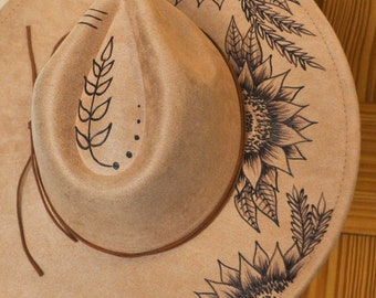 May include: A brown felt fedora hat with a black sunflower and leaf design painted on the brim.