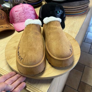 Faith-based engraved slippers with 2 Corinthians 5:7 surrounded by artisan hats and handmade accessories.