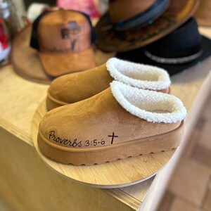 Hand burned Christian Bible verse slippers displayed on wooden stand featuring Proverbs 3:5-6 scripture