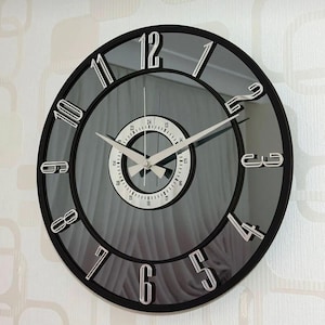May include: A black and silver wall clock with a mirrored face and Roman numeral hour markers. The clock has a second hand and a smaller inner dial.