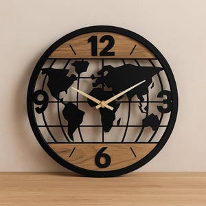 May include: A round wall clock with a black metal frame and a world map design. The clock face features a light wood grain pattern with black numbers at 3, 6, 9, and 12 o'clock. The clock hands are gold-colored.