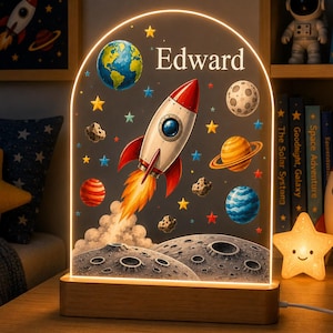 Könnte beinhalten: Ein bogenförmiges Acryl-Nachtlicht mit Holzsockel im Weltraum-Design. Das Motiv zeigt eine Rakete, die Erde, Saturn, einen Mond, Asteroiden und Sterne. Der Name Edward ist in weißer Schrift oben auf der beleuchteten Acrylplatte aufgedruckt.