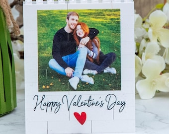 May include: A white Lego-style photo frame with a picture of a couple in a park. The frame has the text "Happy Valentine's Day" and a red heart.