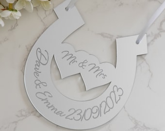 Puede incluir: Una decoración de boda en forma de herradura plateada con el texto "Mr. & Mrs. Dave & Emma 23/09/2023" grabado en ella.