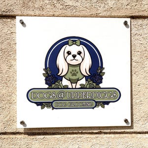 May include: A white square sign with the text "DOGS @ UPPERDIGGS DOG GROOMING". The sign features a cartoon dog with a green paw print on its chest, surrounded by blue roses and a blue and white circular design.