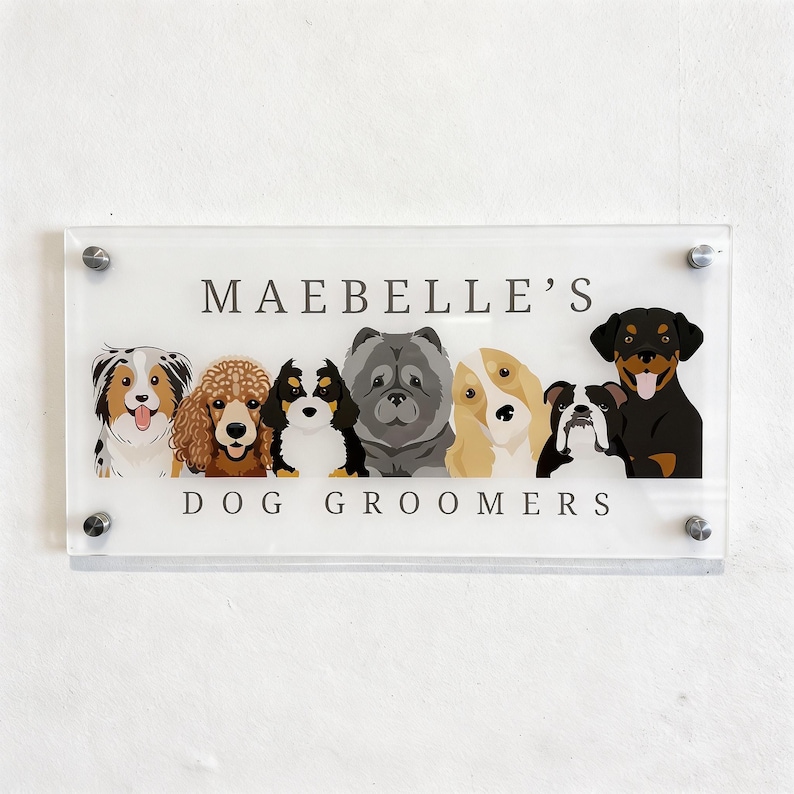 May include: Clear acrylic sign with the text "MAEBBELLE'S DOG GROOMERS" and illustrations of various dog breeds. The sign is mounted with silver hardware and features a white background.