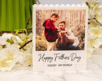 May include: A white block photo frame with a picture of a father and child in a forest setting. The frame has the text "Happy Fathers Day" and "DADDY - MY WORLD" in black script.
