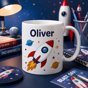 Op de afbeelding: Een witte keramische mok met de naam Oliver in donkerblauwe tekst, voorzien van een kleurrijke illustratie van een raket, een blauwe planeet met ringen, een gele planeet en diverse kleine sterren op een witte achtergrond.