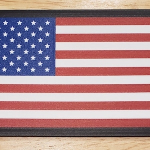 May include: A framed American flag with a black frame. The flag is red, white, and blue with 13 stripes and 50 stars.