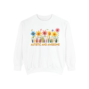 May include: White sweatshirt with a colorful floral design and the text "AUTISTIC AND AWESOME" in orange. The floral design includes various colored flowers, pencils, and butterflies.