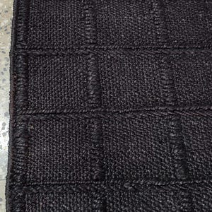 May include: A dark brown rectangular rug featuring a grid pattern of raised, woven squares. The surface is composed of a dense, textured material with a consistent dark brown color throughout, creating a structured and uniform appearance.