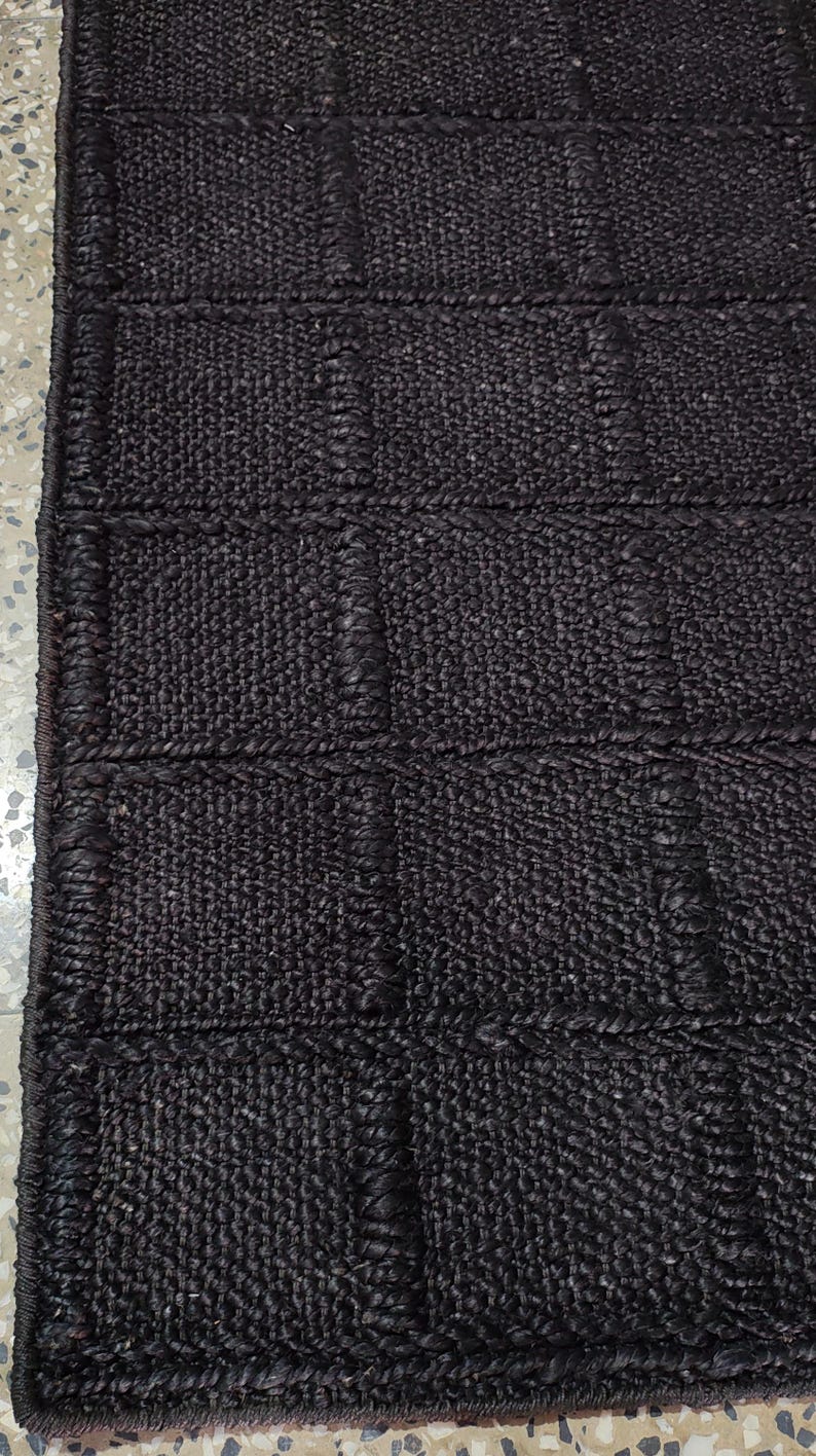 May include: A dark brown rectangular rug featuring a grid pattern of raised, woven squares. The surface is composed of a dense, textured material with a consistent dark brown color throughout, creating a structured and uniform appearance.