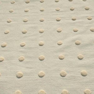 May include: A cream-coloured textile featuring a repeating pattern of raised, circular tufted dots in a matching cream hue. The fabric has a visible woven texture, and the dots are arranged in a consistent grid across the entire surface.
