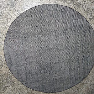 May include: A circular rug featuring a dense, woven texture in a monochromatic black and white colour scheme. The surface displays a fine, cross-hatched pattern created by the interlacing of dark and light threads, resulting in a grey appearance.