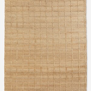 Puede incluir: Alfombra rectangular de yute tejido con un patr&oacute;n de cuadr&iacute;cula. La alfombra es de color beige natural, con una sutil variaci&oacute;n de tono en la superficie. La cuadr&iacute;cula est&aacute; formada por l&iacute;neas ligeramente elevadas y m&aacute;s oscuras, creando un efecto texturizado.