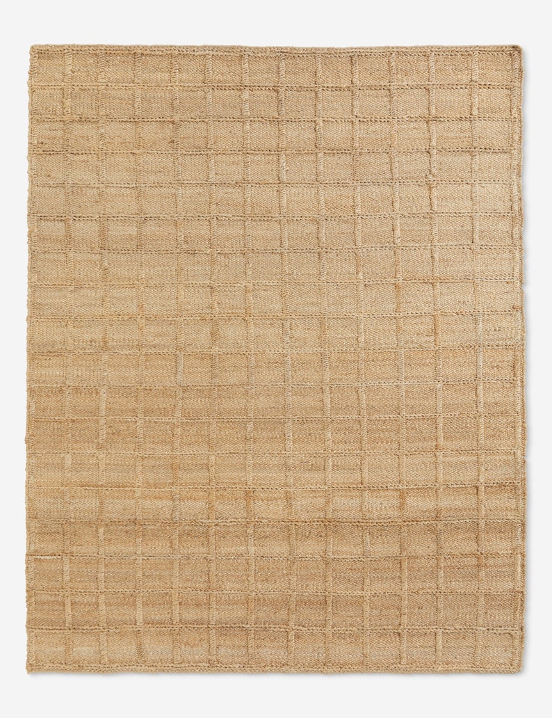 Puede incluir: Alfombra rectangular de yute tejido con un patr&oacute;n de cuadr&iacute;cula. La alfombra es de color beige natural, con una sutil variaci&oacute;n de tono en la superficie. La cuadr&iacute;cula est&aacute; formada por l&iacute;neas ligeramente elevadas y m&aacute;s oscuras, creando un efecto texturizado.