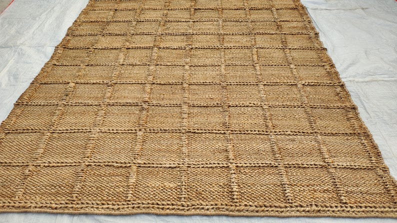May include: A rectangular area rug crafted from natural tan fibers, featuring a prominent grid pattern created by raised, woven lines that form uniform squares across the entire surface of the textured, earthy-toned floor covering.